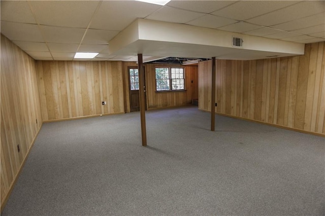 basement with wooden walls, a paneled ceiling, and light colored carpet