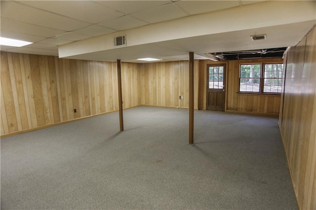 basement featuring carpet, a drop ceiling, and wooden walls