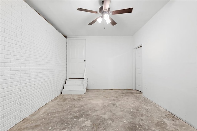 empty room with brick wall, unfinished concrete flooring, and ceiling fan