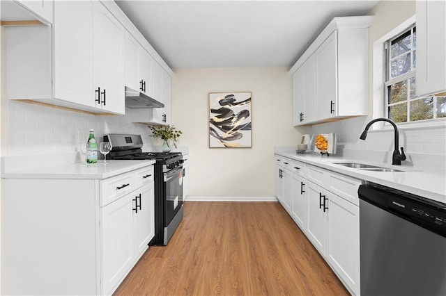 kitchen featuring decorative backsplash, under cabinet range hood, a sink, light wood-style flooring, and stainless steel appliances