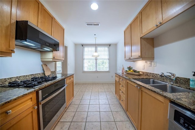 kitchen featuring stone counters, decorative light fixtures, light tile patterned floors, stainless steel appliances, and a sink