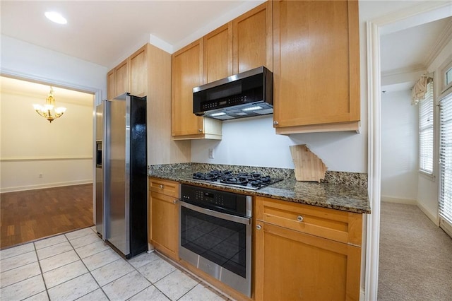 kitchen with light tile patterned floors, stainless steel appliances, baseboards, dark stone countertops, and an inviting chandelier