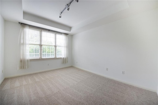 unfurnished room featuring track lighting, a raised ceiling, light carpet, and baseboards