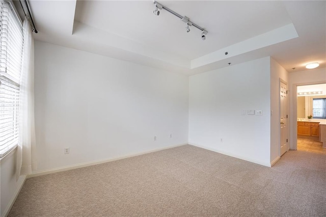 empty room featuring light carpet, baseboards, and a raised ceiling