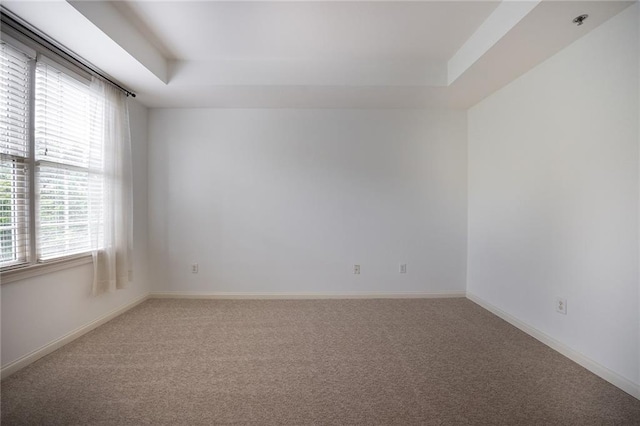 carpeted empty room with a tray ceiling and baseboards