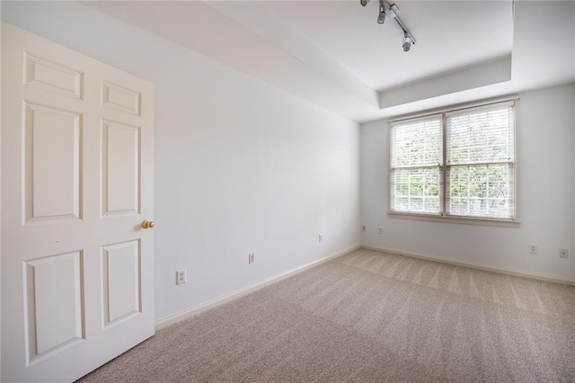 spare room featuring rail lighting, baseboards, light colored carpet, and a tray ceiling