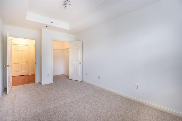 unfurnished bedroom featuring light colored carpet, baseboards, a closet, a raised ceiling, and track lighting