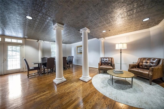 living area featuring ornate columns, baseboards, ornamental molding, and wood finished floors