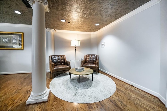 living area with ornate columns, baseboards, ornamental molding, and wood finished floors