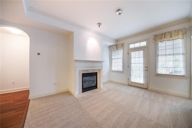 unfurnished living room with baseboards, a premium fireplace, arched walkways, and crown molding