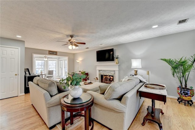 living room with a fireplace, a textured ceiling, ceiling fan, and light hardwood / wood-style floors