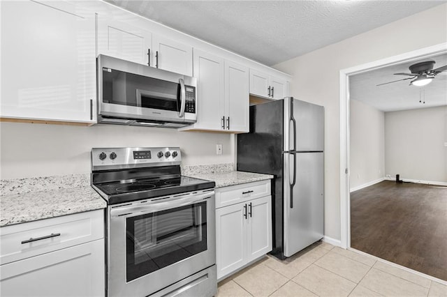 kitchen featuring light tile patterned floors, light stone countertops, stainless steel appliances, white cabinets, and a textured ceiling