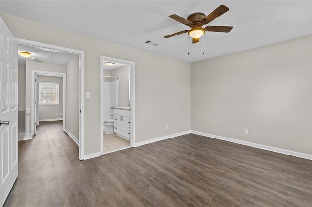 unfurnished bedroom featuring visible vents, baseboards, attic access, wood finished floors, and a ceiling fan