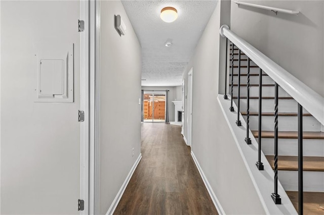 corridor featuring baseboards, a textured ceiling, wood finished floors, and stairs
