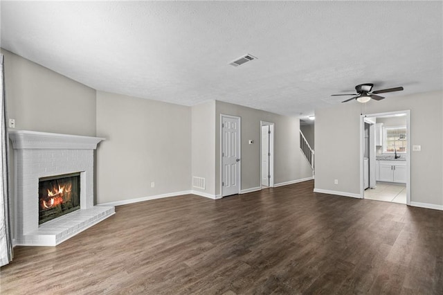 unfurnished living room with a ceiling fan, a brick fireplace, dark wood-style floors, and visible vents