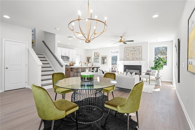 dining room with ceiling fan with notable chandelier, light hardwood / wood-style floors, a wealth of natural light, and sink