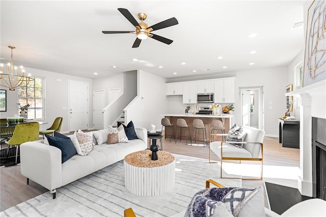 living room featuring ceiling fan with notable chandelier and light wood-type flooring