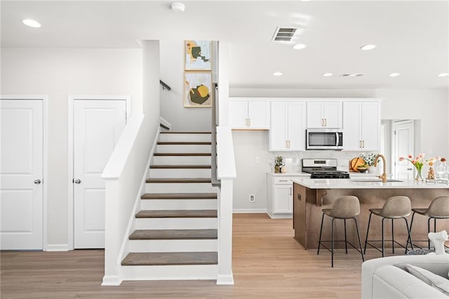 kitchen with a breakfast bar, white cabinets, stainless steel appliances, and light hardwood / wood-style floors