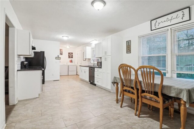 kitchen featuring decorative backsplash, sink, separate washer and dryer, black dishwasher, and white cabinetry