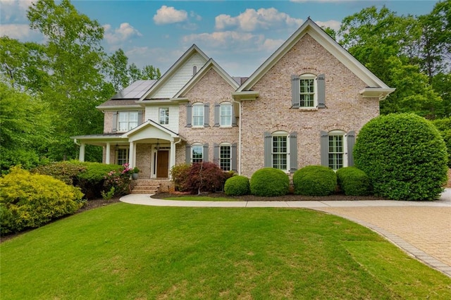 view of front of property featuring a porch, brick siding, solar panels, and a front lawn