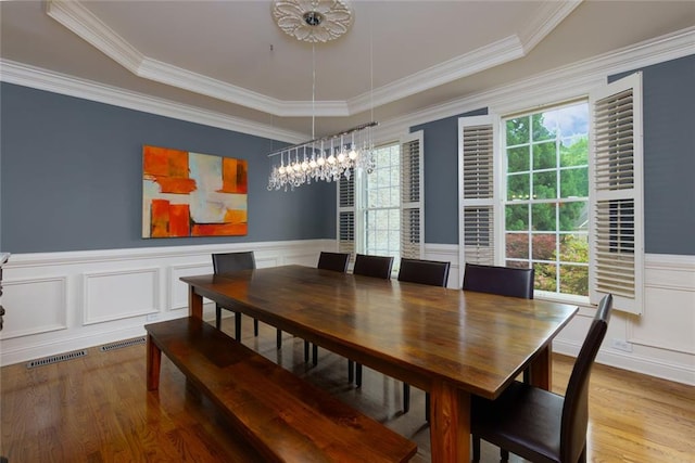 dining room with visible vents, wood finished floors, a notable chandelier, ornamental molding, and a decorative wall