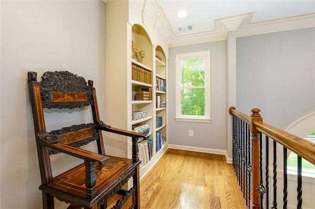 hall with visible vents, ornamental molding, light wood-style flooring, and an upstairs landing