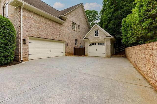 view of side of property featuring driveway, a garage, brick siding, fence, and a shingled roof