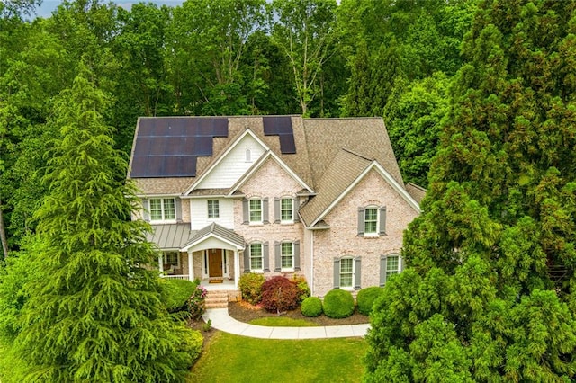 view of front of property with a shingled roof, a front lawn, covered porch, and solar panels