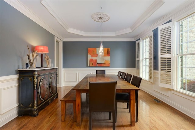 dining space with a healthy amount of sunlight, a decorative wall, wood finished floors, and visible vents