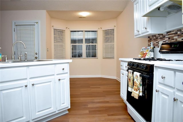 kitchen with range hood, white cabinetry, light hardwood / wood-style floors, and white gas stove