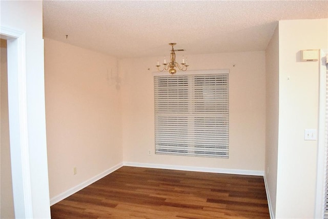 unfurnished room featuring an inviting chandelier, a textured ceiling, and dark hardwood / wood-style floors