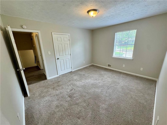 unfurnished bedroom with baseboards, visible vents, a textured ceiling, and carpet