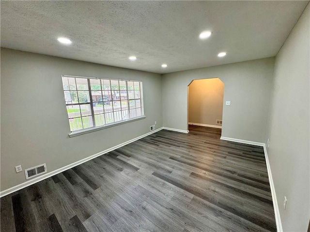 unfurnished room featuring visible vents, arched walkways, dark wood-type flooring, and recessed lighting