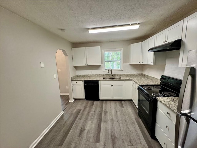 kitchen featuring light wood-style floors, under cabinet range hood, white cabinets, black appliances, and a sink