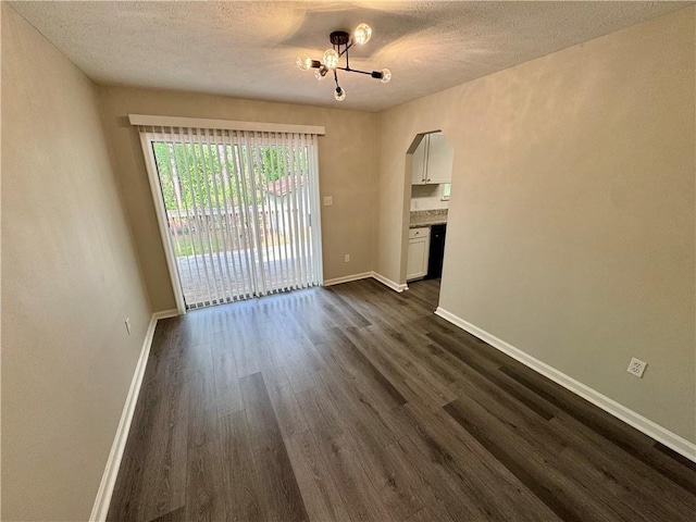 spare room with a textured ceiling, a notable chandelier, dark wood-style floors, and arched walkways