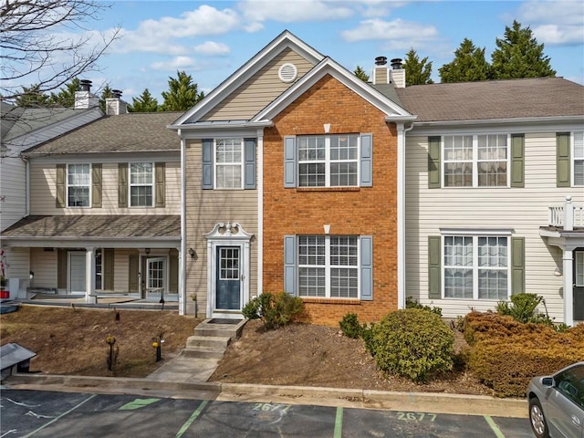 multi unit property featuring brick siding, a shingled roof, a chimney, and uncovered parking