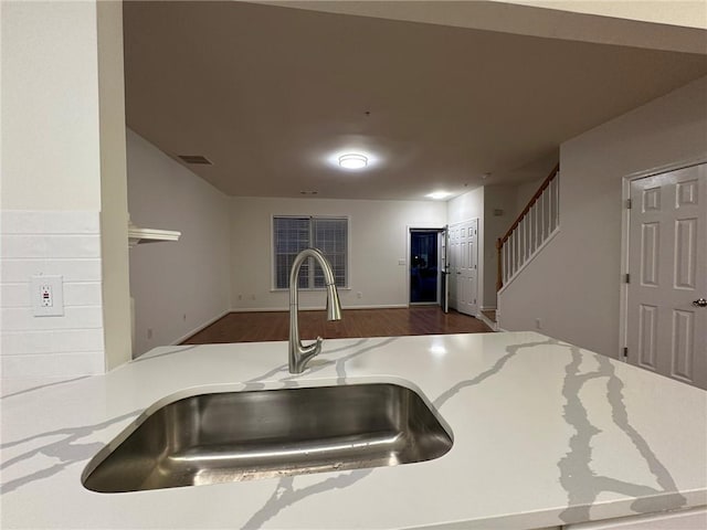 kitchen with visible vents, light stone countertops, open floor plan, wood finished floors, and a sink