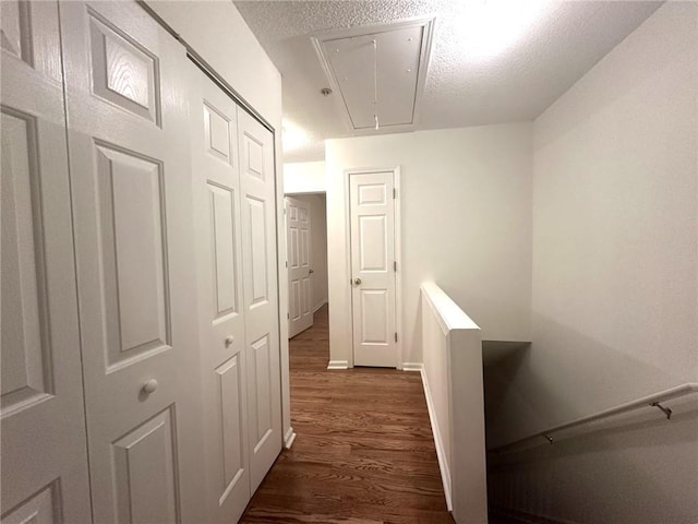 hall with baseboards, attic access, dark wood-style flooring, a textured ceiling, and an upstairs landing