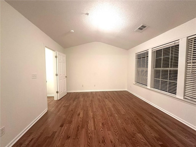 unfurnished room with baseboards, visible vents, dark wood finished floors, vaulted ceiling, and a textured ceiling