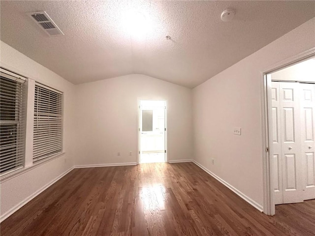 interior space featuring visible vents, dark wood-type flooring, baseboards, lofted ceiling, and a textured ceiling