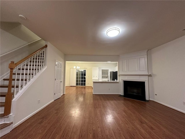 unfurnished living room featuring a large fireplace, baseboards, dark wood finished floors, stairs, and an inviting chandelier