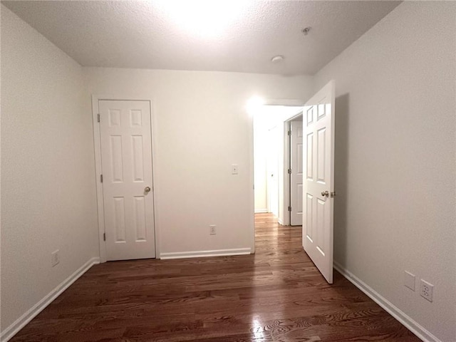 unfurnished bedroom with a textured ceiling, baseboards, and wood finished floors