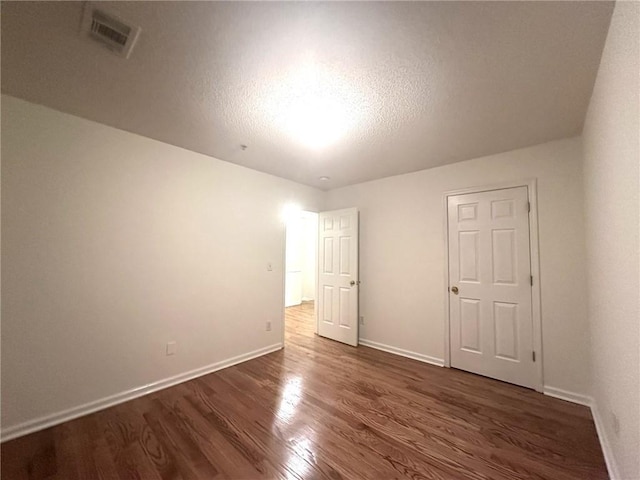 unfurnished bedroom featuring dark wood finished floors, visible vents, a textured ceiling, and baseboards