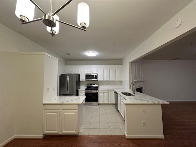 kitchen with light wood-style flooring, a sink, white cabinetry, appliances with stainless steel finishes, and a peninsula