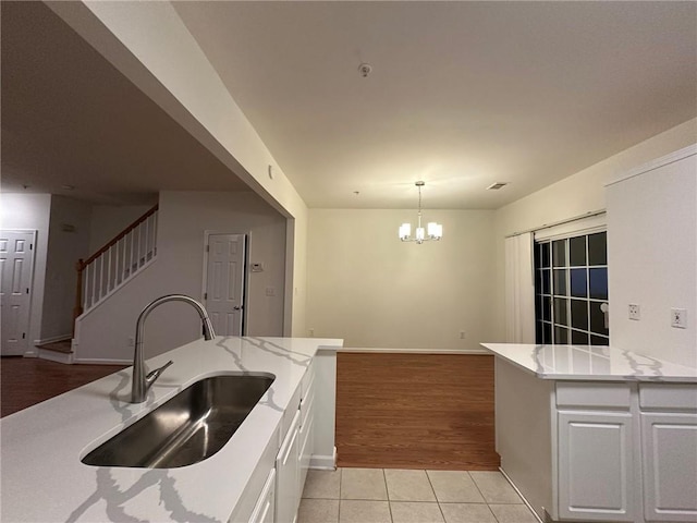 kitchen featuring light stone countertops, light tile patterned flooring, a notable chandelier, white cabinets, and a sink