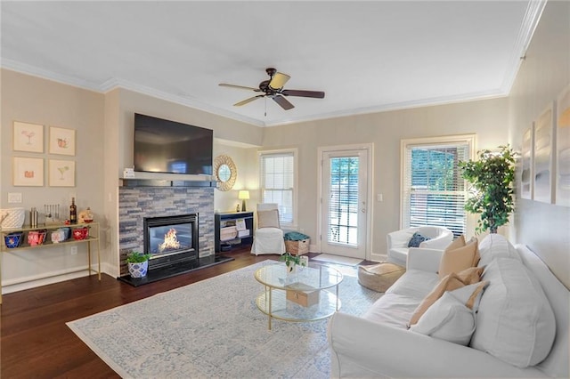 living room with ceiling fan, crown molding, dark hardwood / wood-style flooring, and a stone fireplace