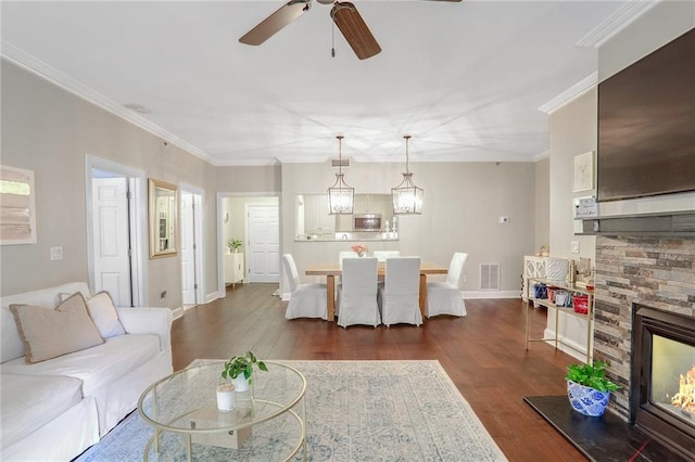 living room featuring ceiling fan, a stone fireplace, dark hardwood / wood-style floors, and ornamental molding