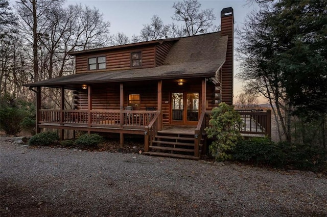 cabin with a shingled roof, log exterior, covered porch, and a chimney