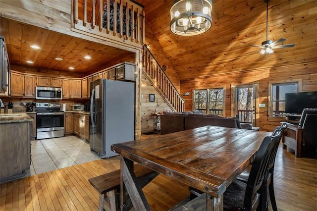 dining space featuring wooden walls, high vaulted ceiling, stairs, wood ceiling, and light wood-type flooring