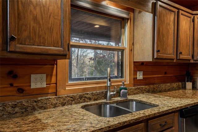 kitchen featuring stone counters, brown cabinets, dishwasher, and a sink